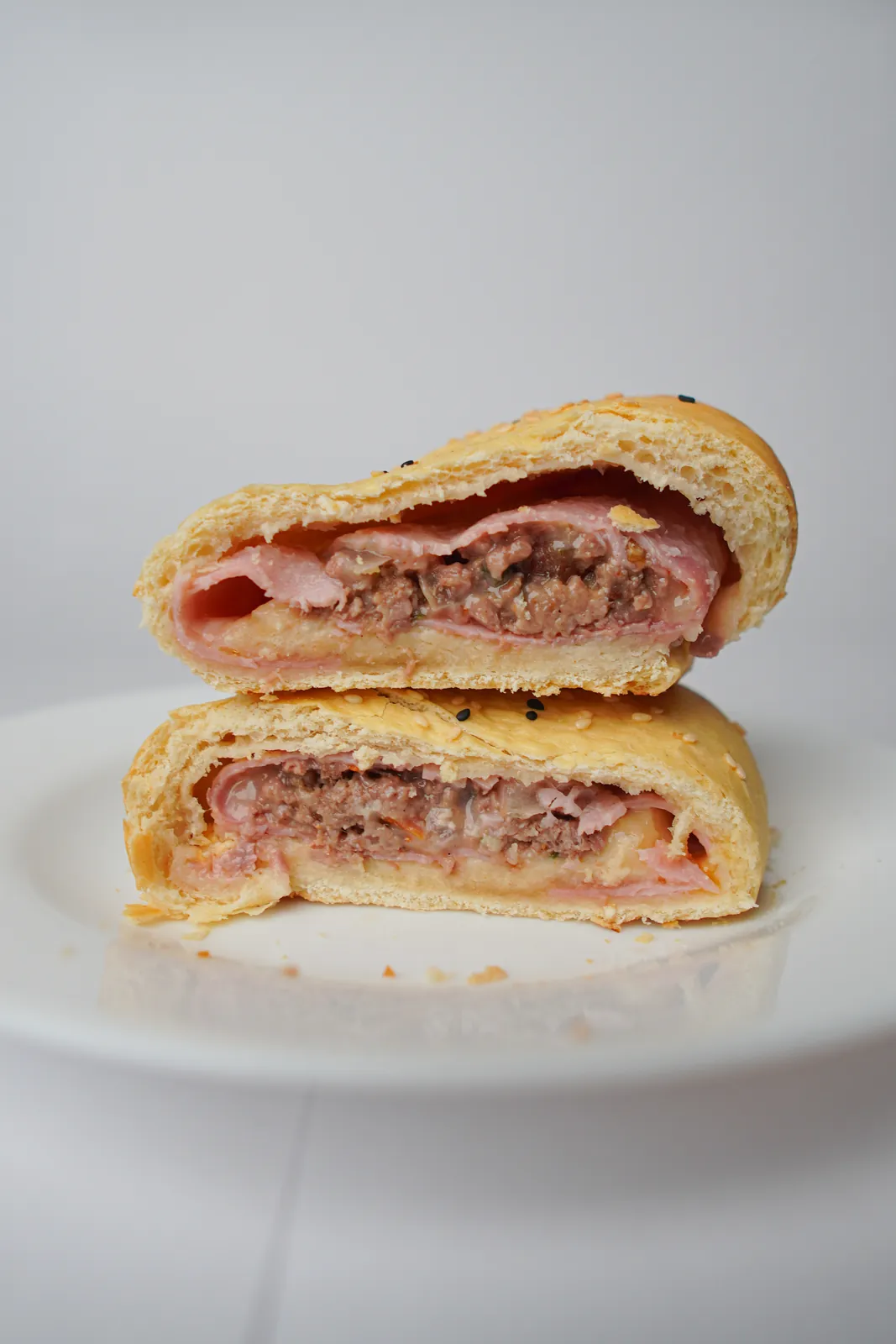 Assado de carne, presunto e queijo no pão de leite aberto ao meio, num prato branco