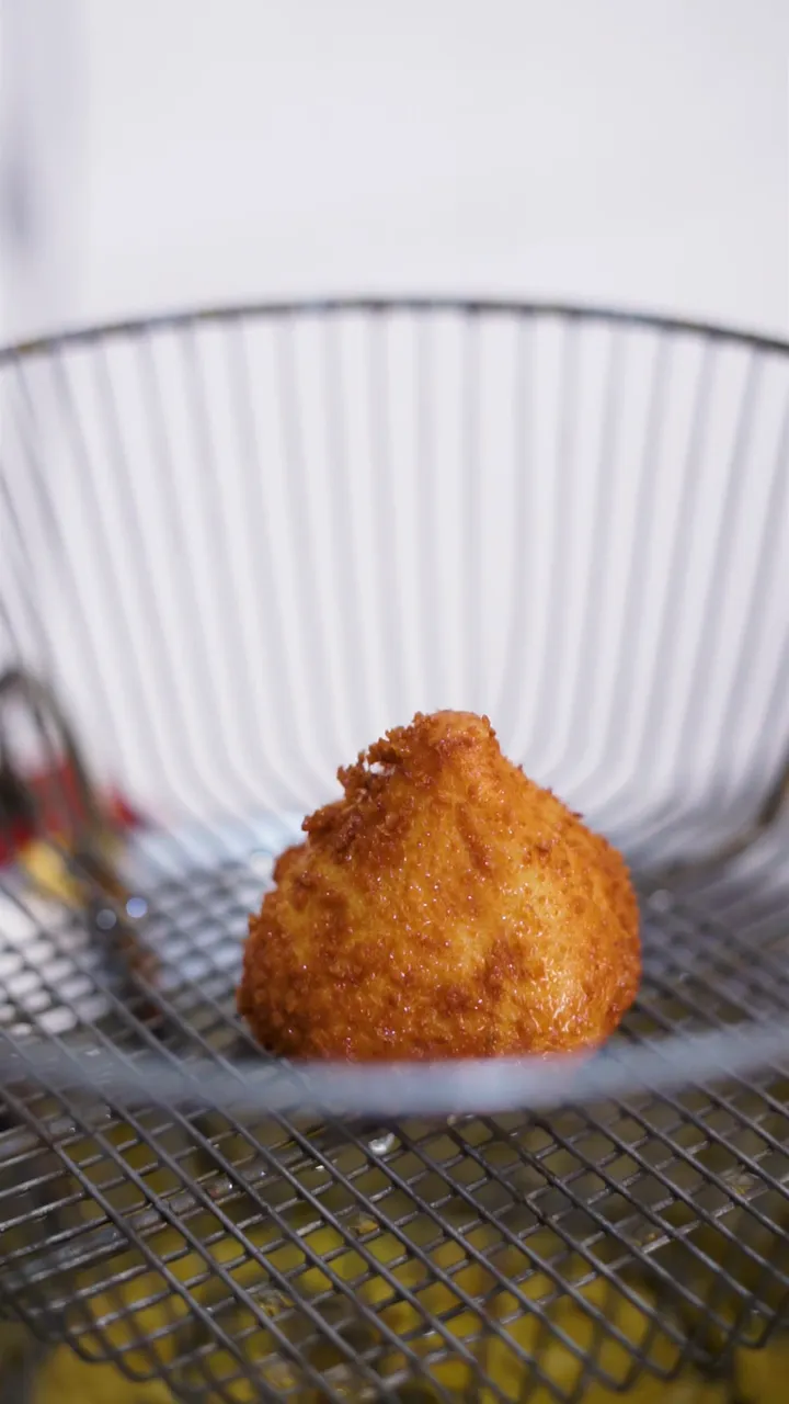 Coxinha dourada recém-saída da fritura no cesto de arame
