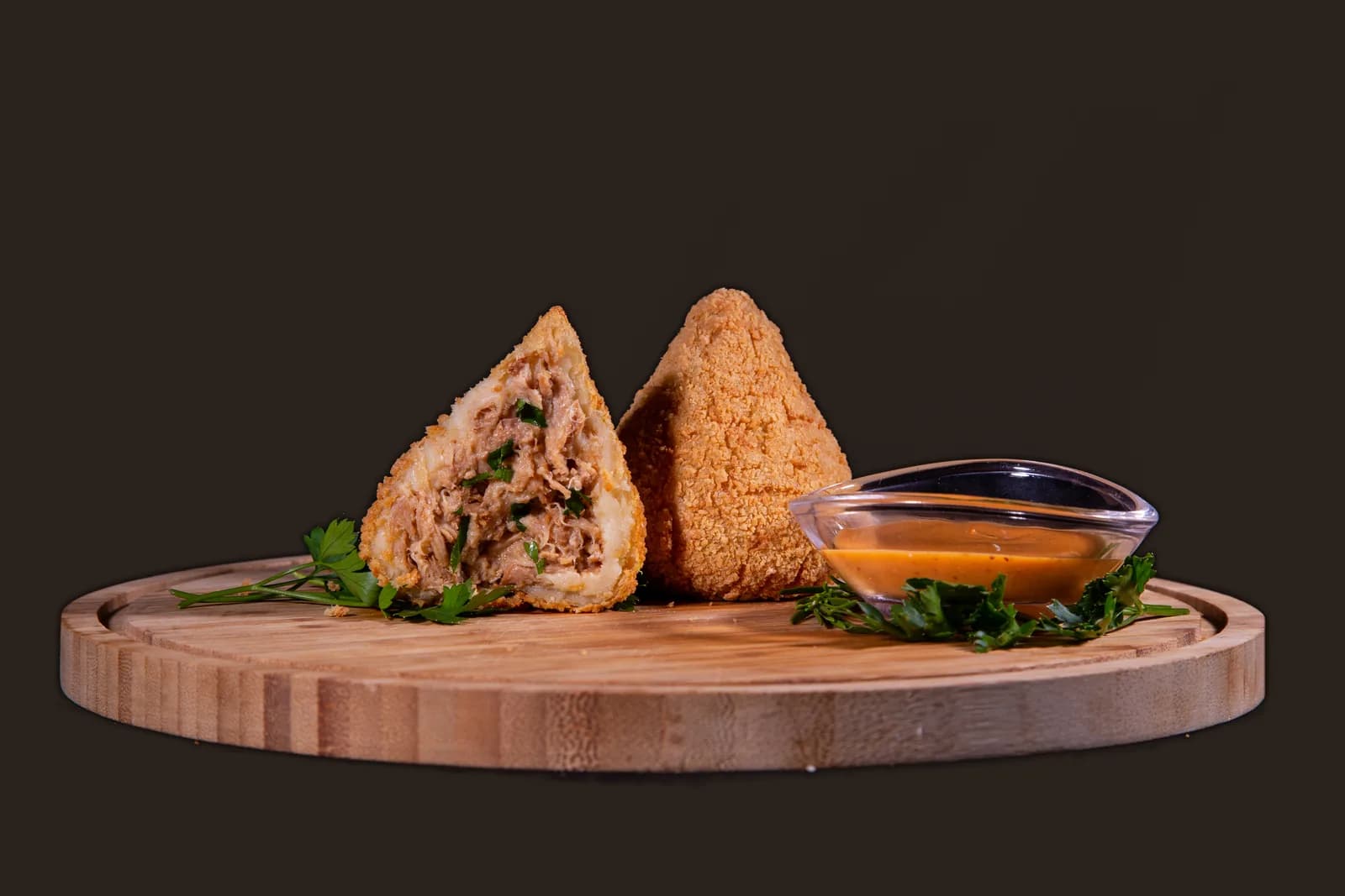 Coxinha de pernil aberta ao lado de uma inteira, numa tábua de madeira