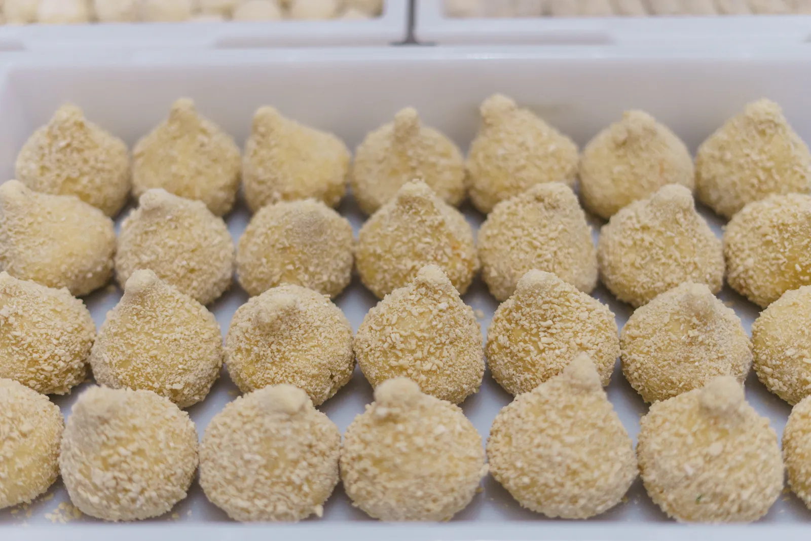 Detalhe das coxinhas empanadas à mão, prontas para fritar