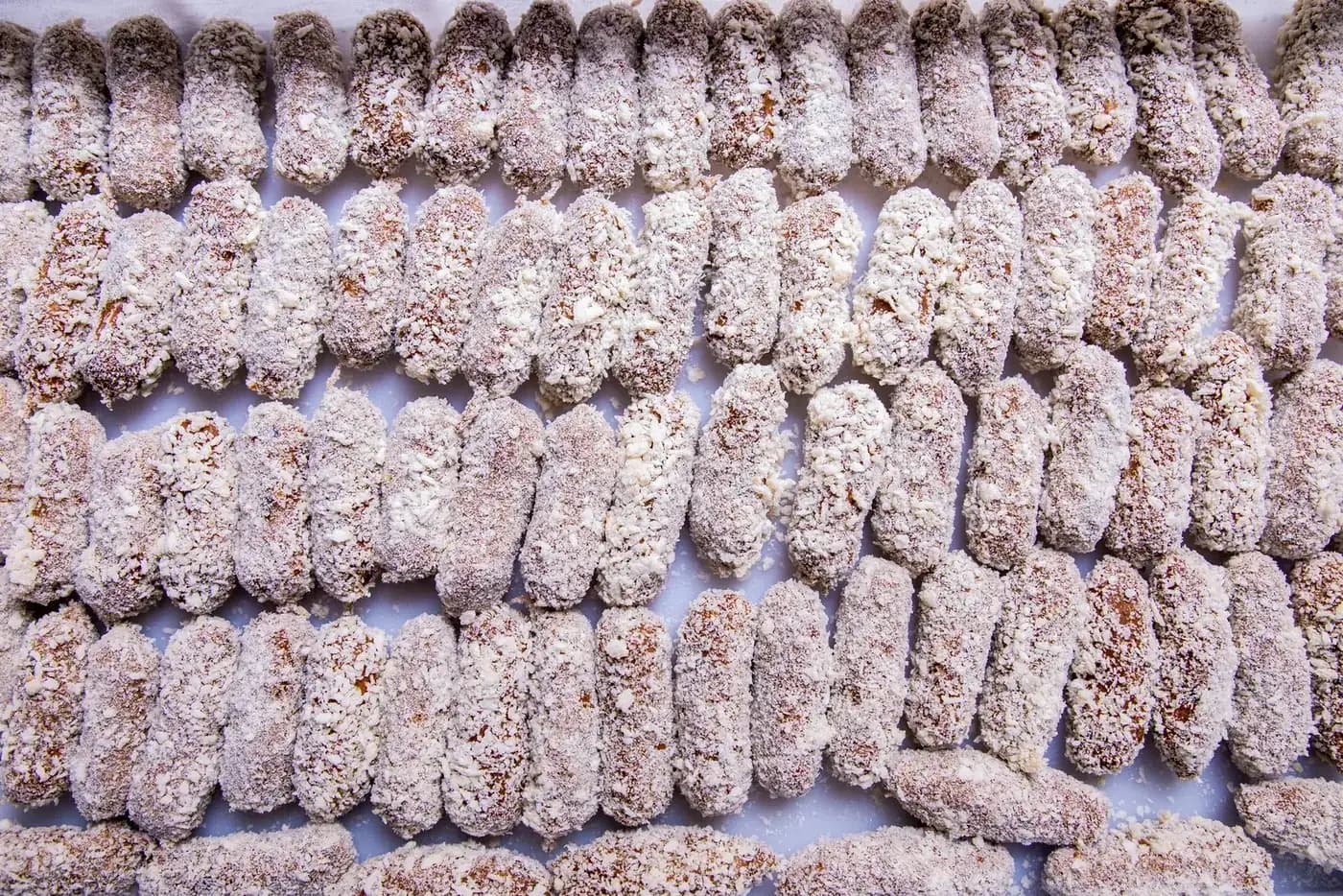 Salgados empanados crus em fileiras numa bandeja