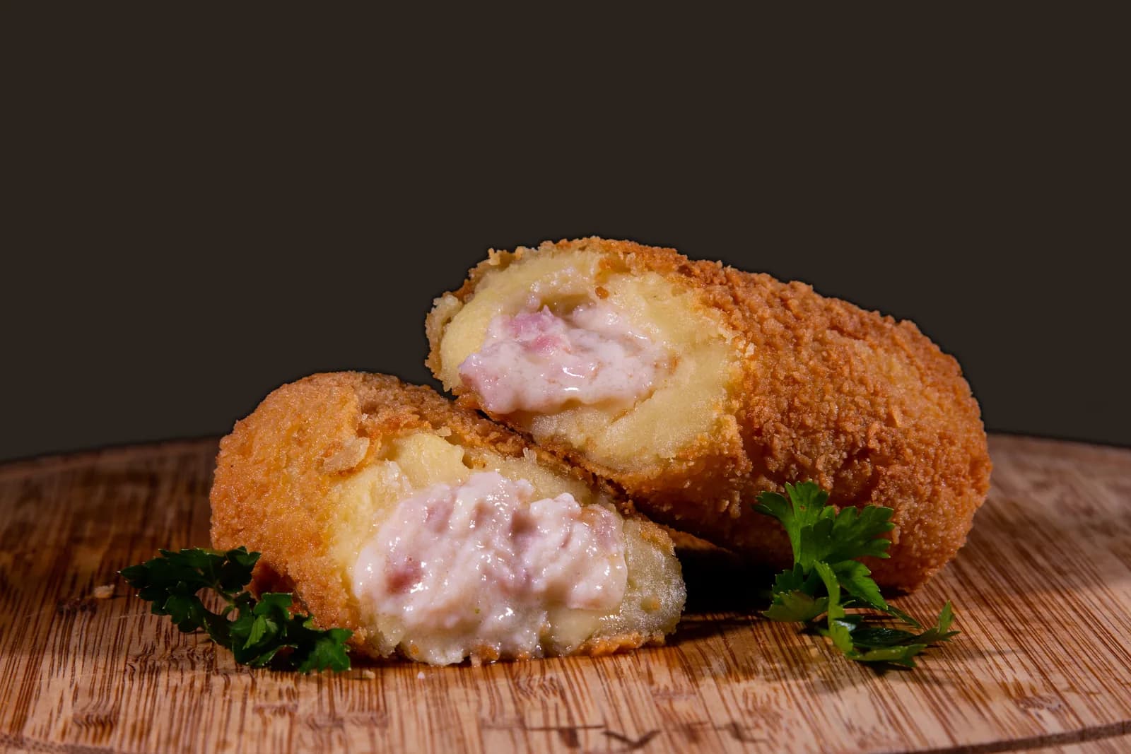 Enrolado de presunto e queijo aberto ao lado de outro, numa tábua de madeira