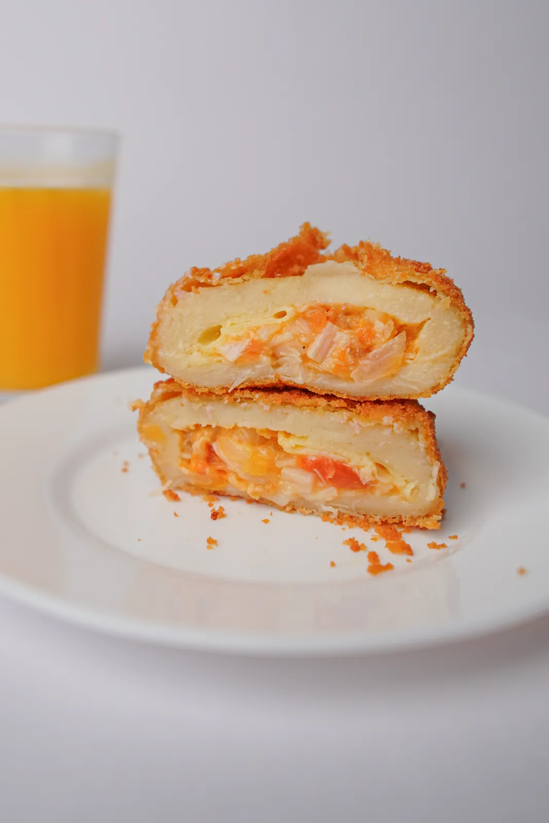 Salgado de palmito com mussarela aberto ao meio, num prato, com um copo de suco ao fundo