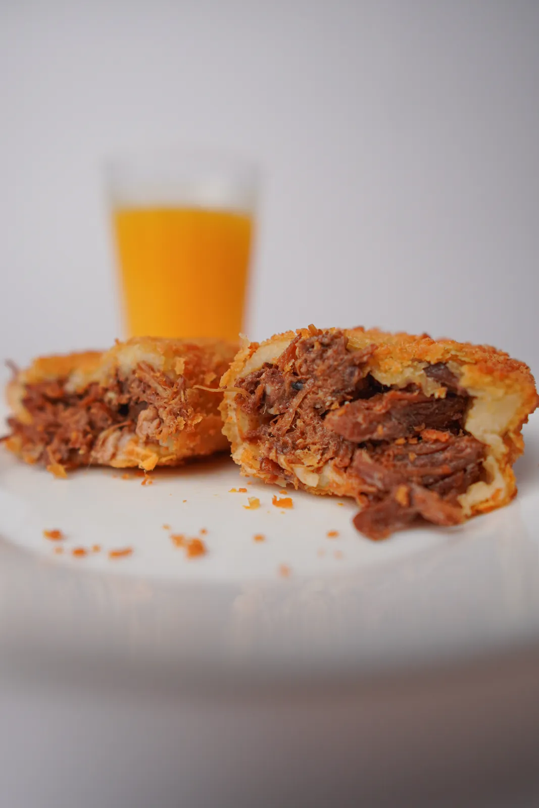 Risoles de carne de panela aberto ao meio, num prato, com um copo de suco ao fundo