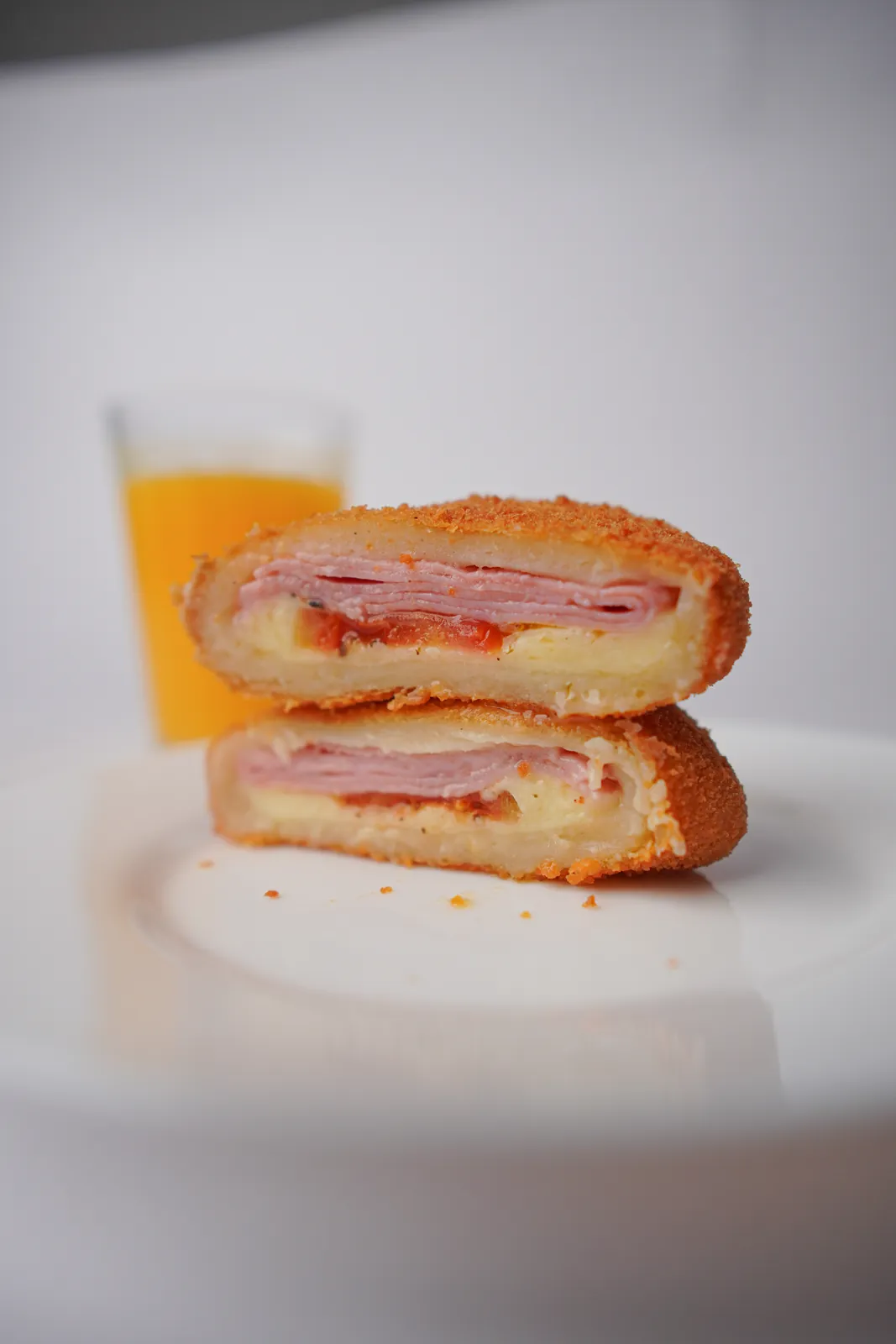 Salgado de pizza aberto ao meio, num prato, com um copo de suco ao fundo