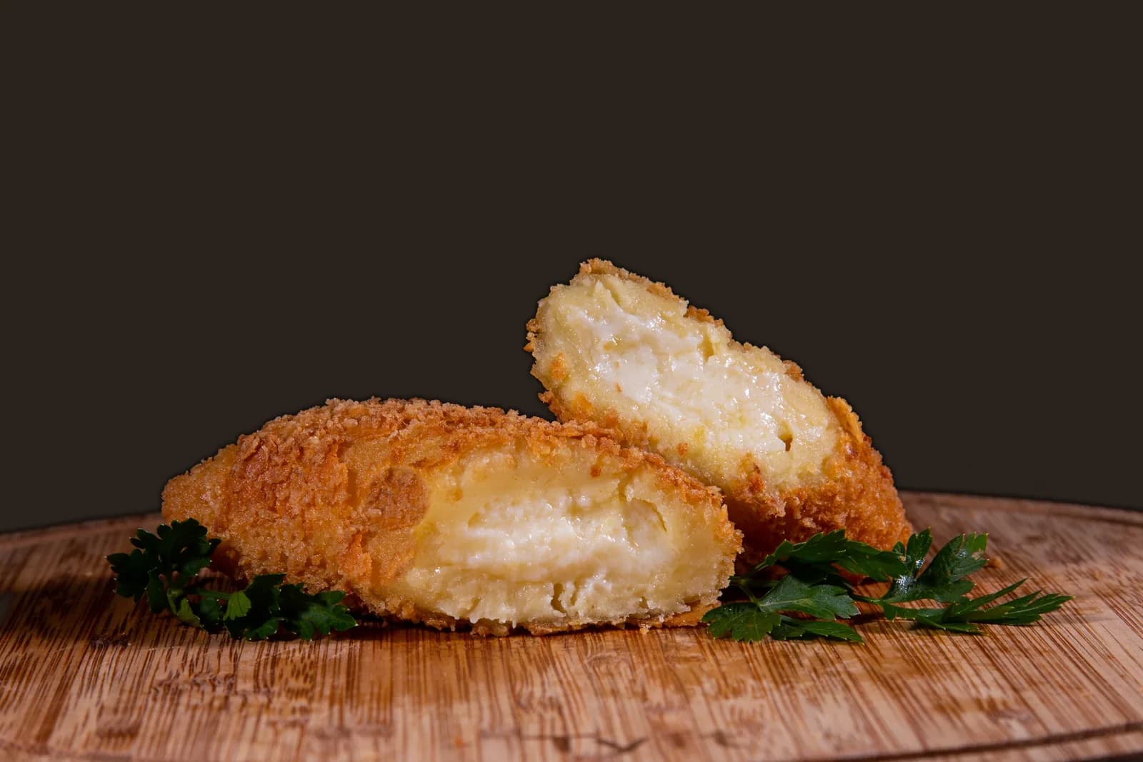 Travesseiro de queijo aberto ao lado de outro, com o queijo cremoso à mostra, numa tábua de madeira